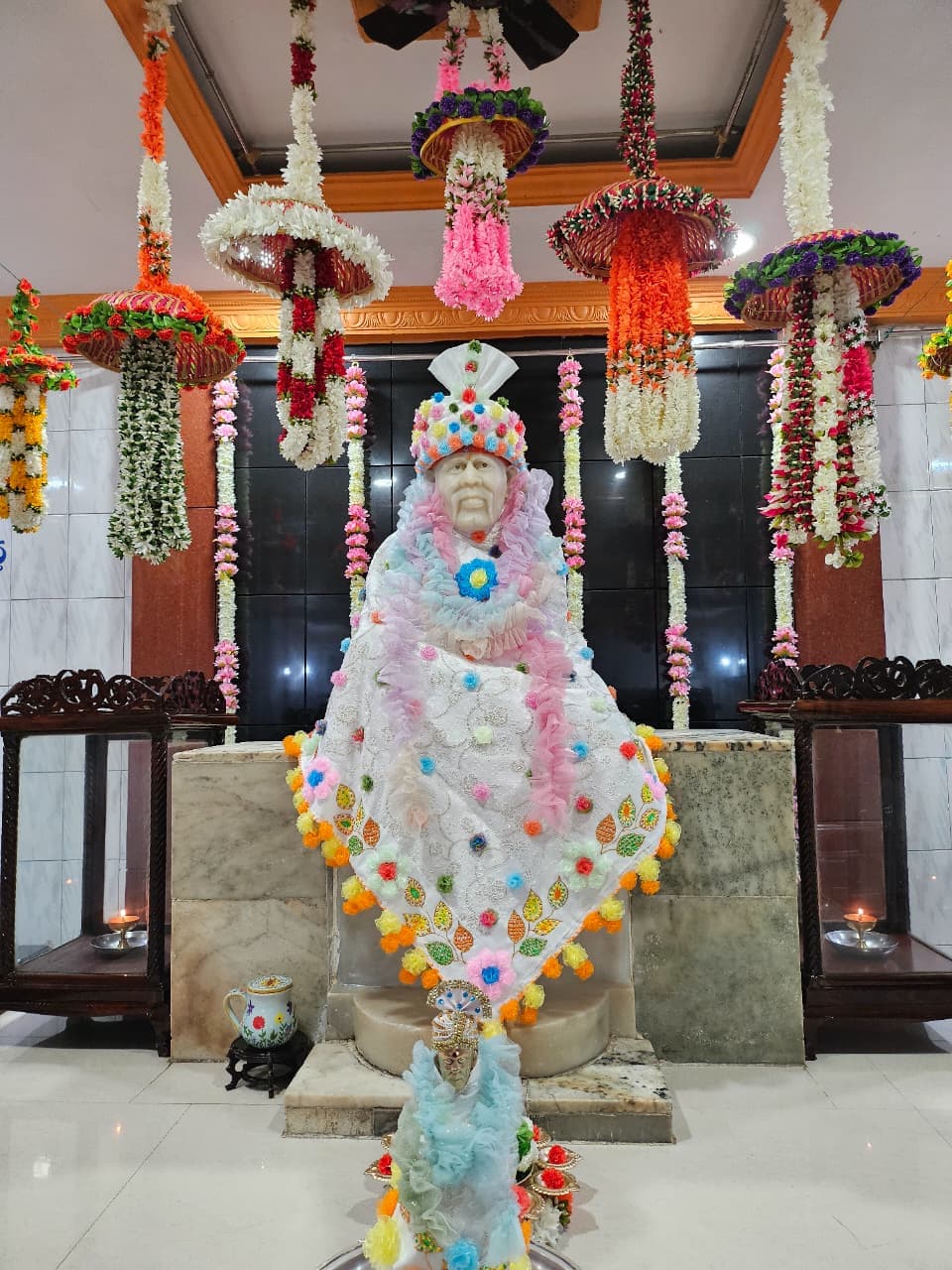 Close view of the murti's face, beaded floral crown, and multicolor poncho