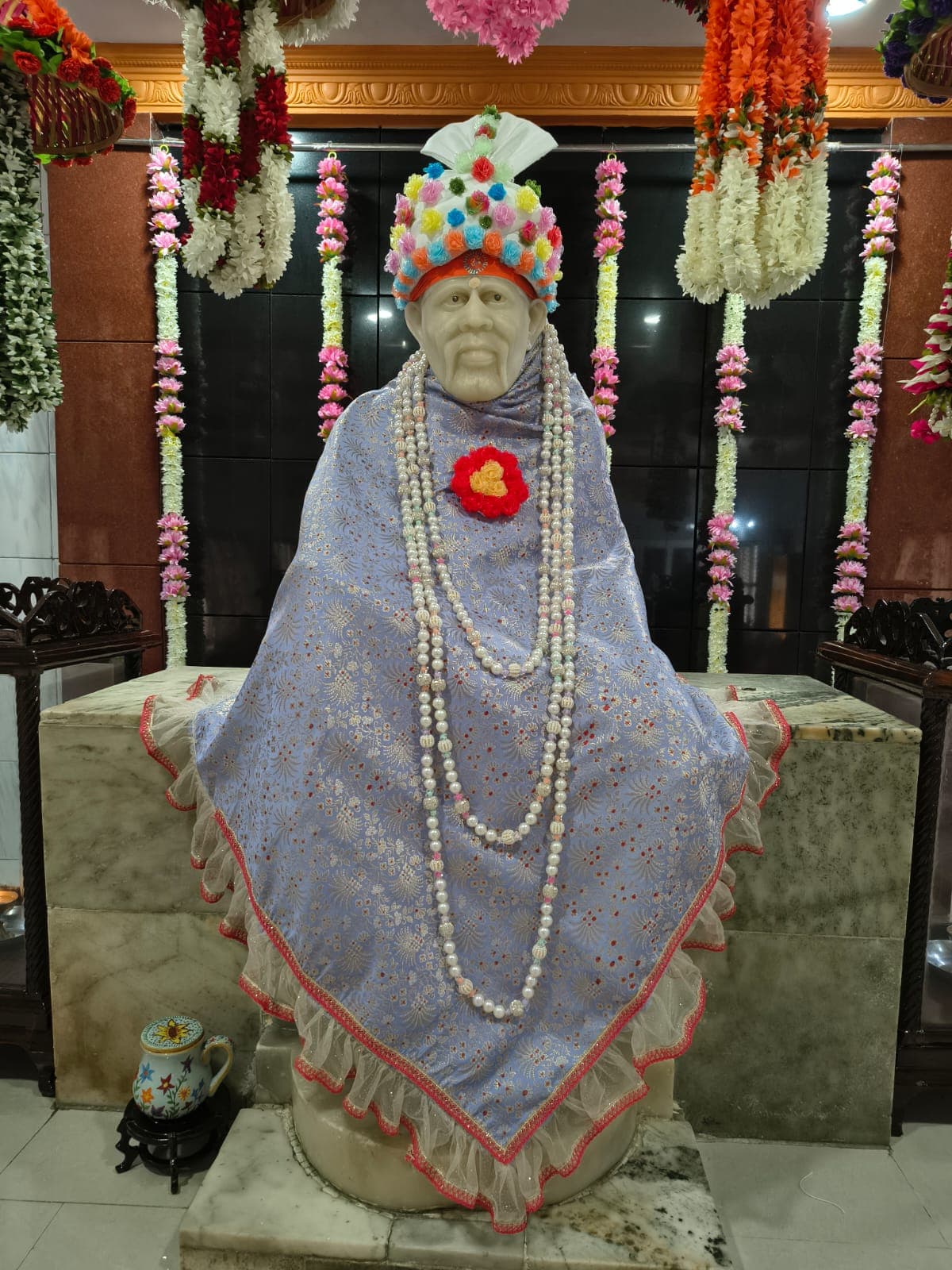 The murti dressed in a purple floral-brocade shawl with layered pearl garlands
