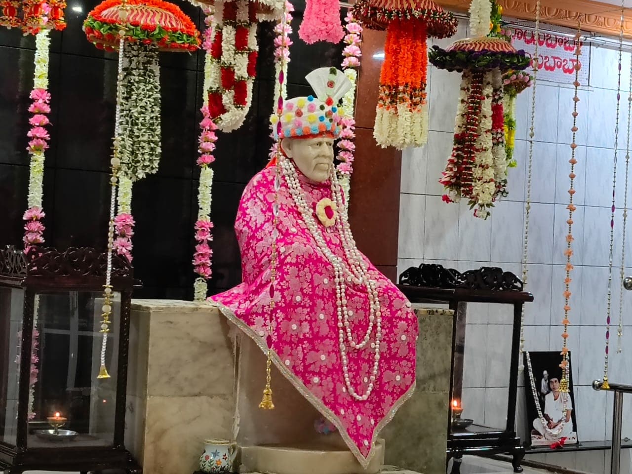 Wide view of the murti dressed in a bright pink shawl, framed by hanging garlands throughout the sanctum