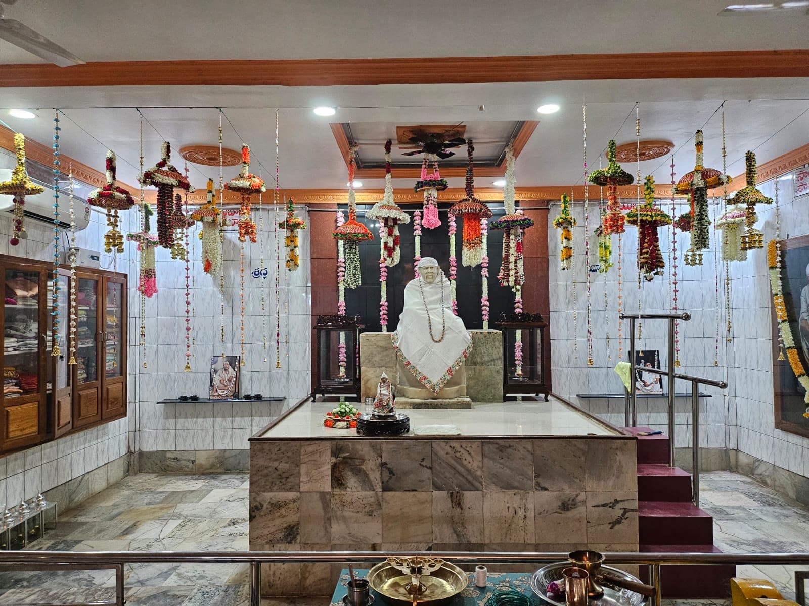 Wide view of the sanctum decorated for Dasara, with elaborate hanging floral garlands and a large bell, the murti dressed in a plain white shawl