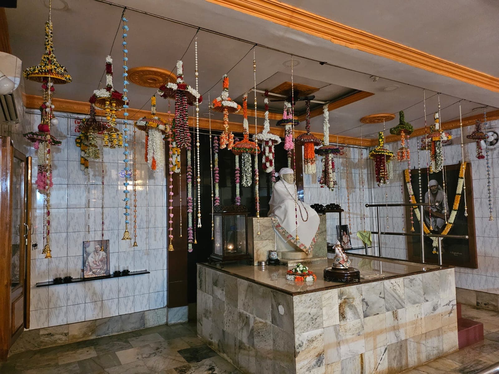 The murti in a plain white shawl, seen from the side of the sanctum with the Shraddha signage visible on the wall