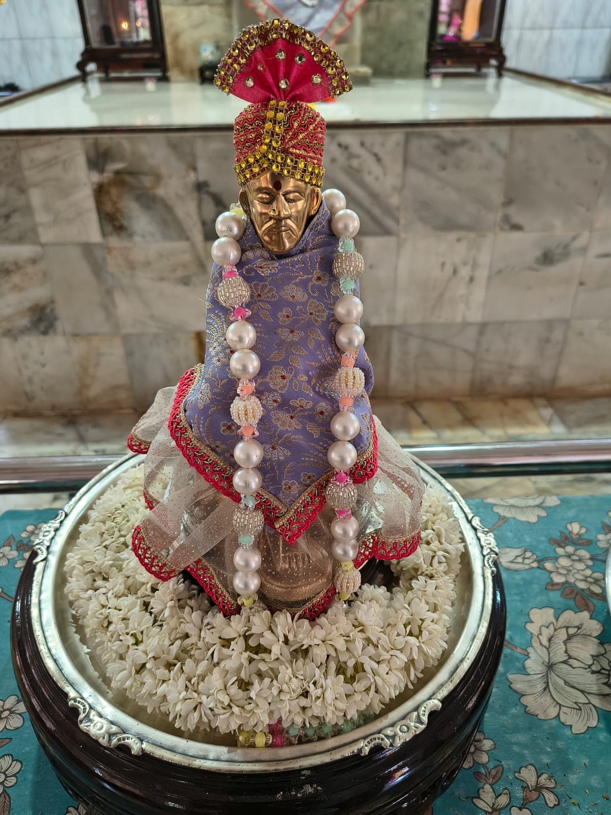 The temple's small murti dressed in a blue and gold shawl with pearl garlands, set in a bed of jasmine flowers