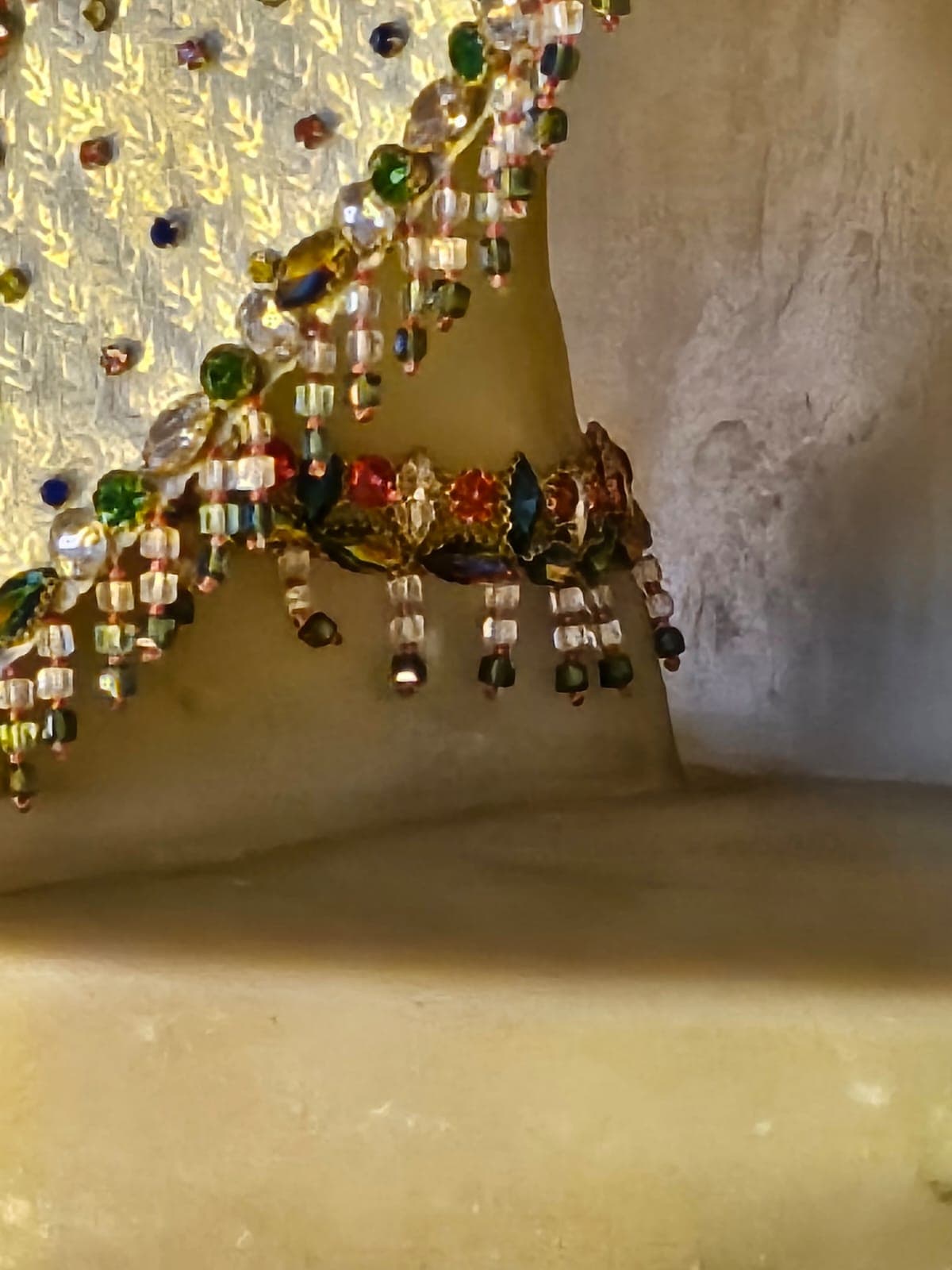 Close-up of a jeweled anklet on the murti's foot, with dangling beaded tassels