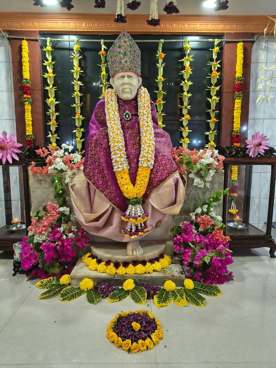 The murti in the purple and gold shawl and jeweled crown, flanked by bougainvillea flowers in pink and white