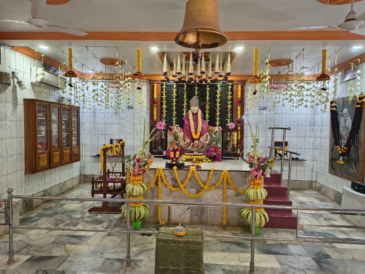 Wide view of the sanctum with the large altar bell overhead, the murti in the purple and gold shawl seen at the distant altar