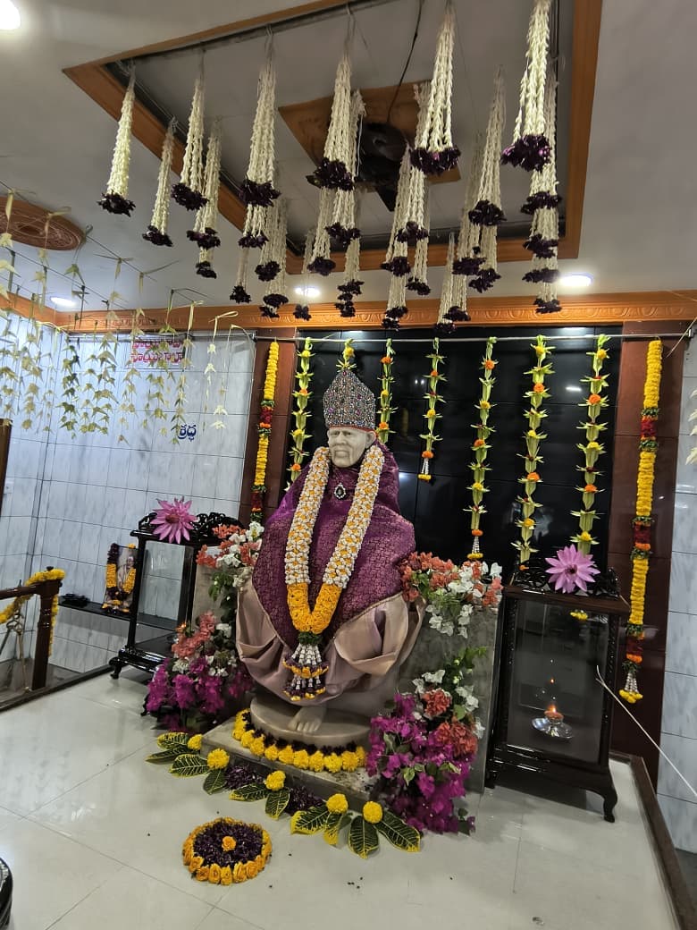 Wide view from the ceiling garlands down to the altar, the murti dressed in the purple and gold shawl amid bougainvillea flowers