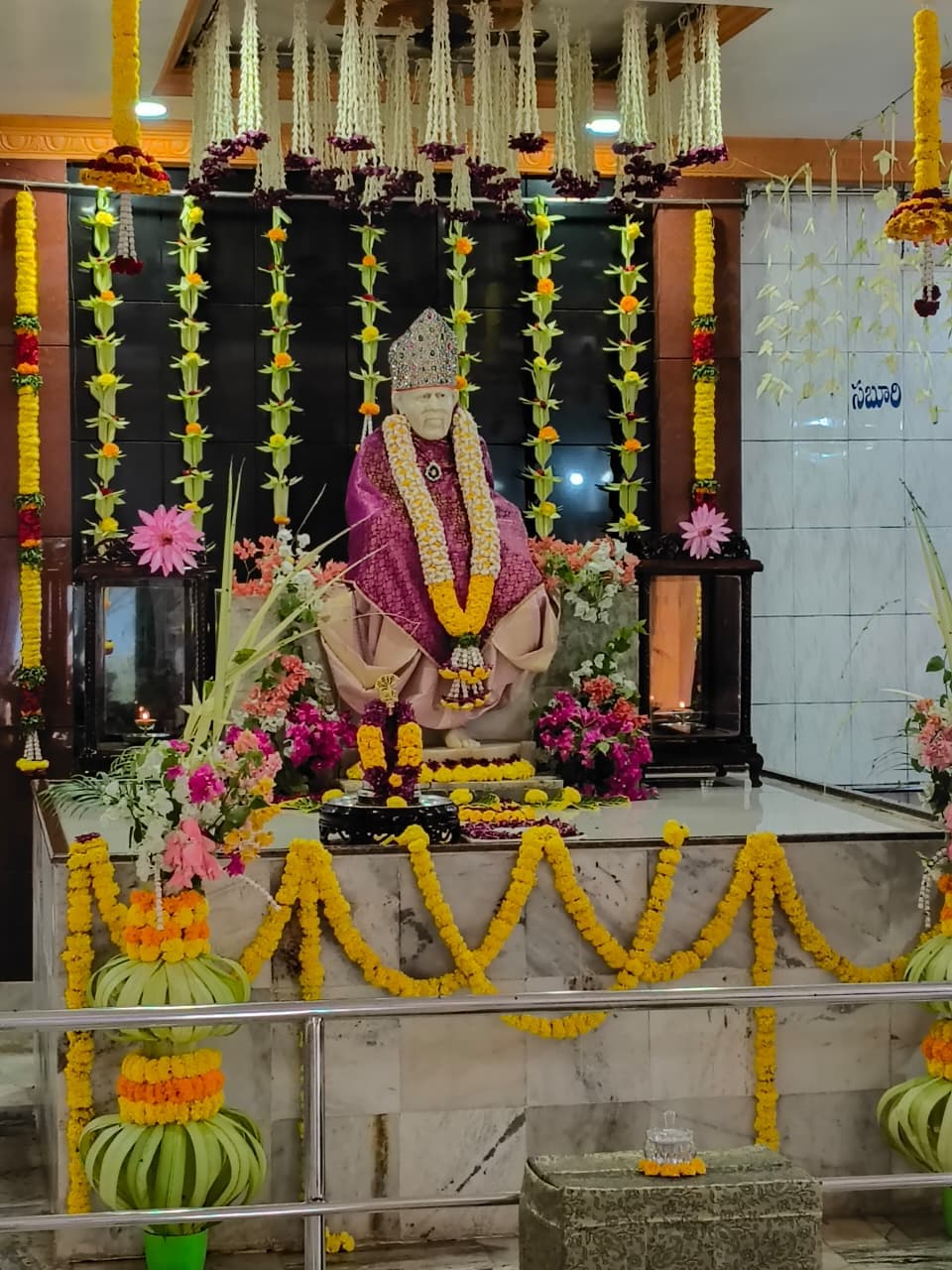 Another wide view of the sanctum, marigold garland topiaries at the railing and the murti in purple and gold at the altar