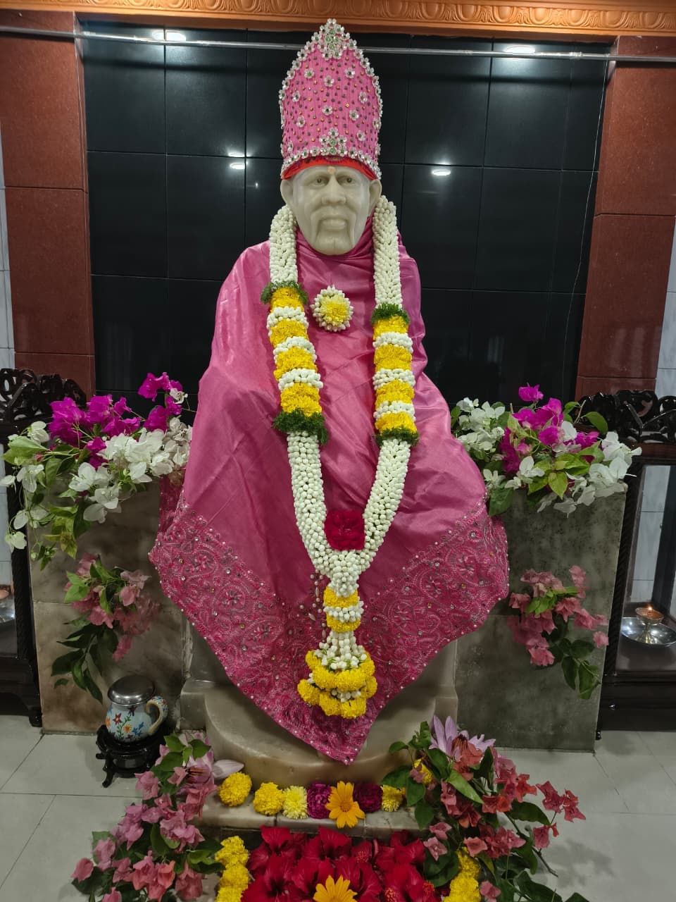 Murti dressed in a pink silk robe with a jeweled crown and a white-and-yellow marigold garland