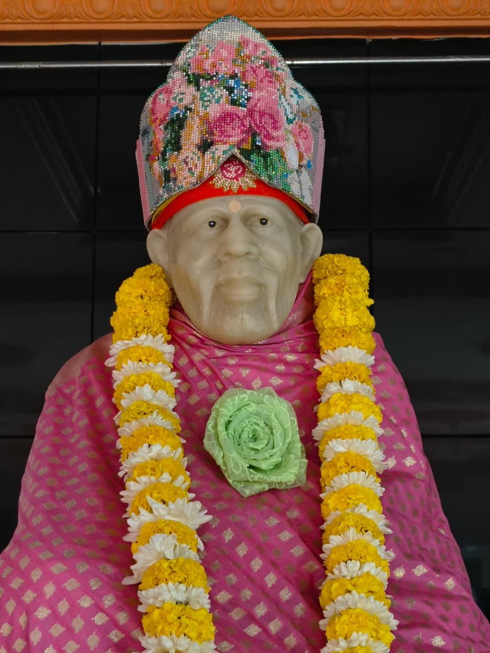 Murti in a pink brocade robe with a beaded rose-pattern crown and a marigold garland