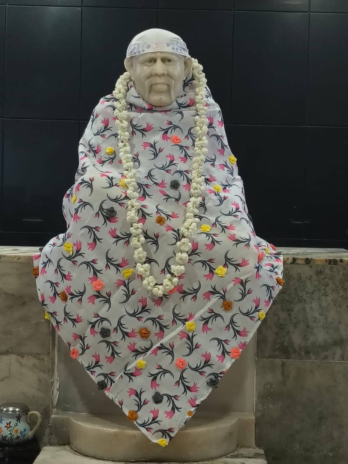 Murti wearing a white floral-print shawl with fabric rose accents and a white flower garland