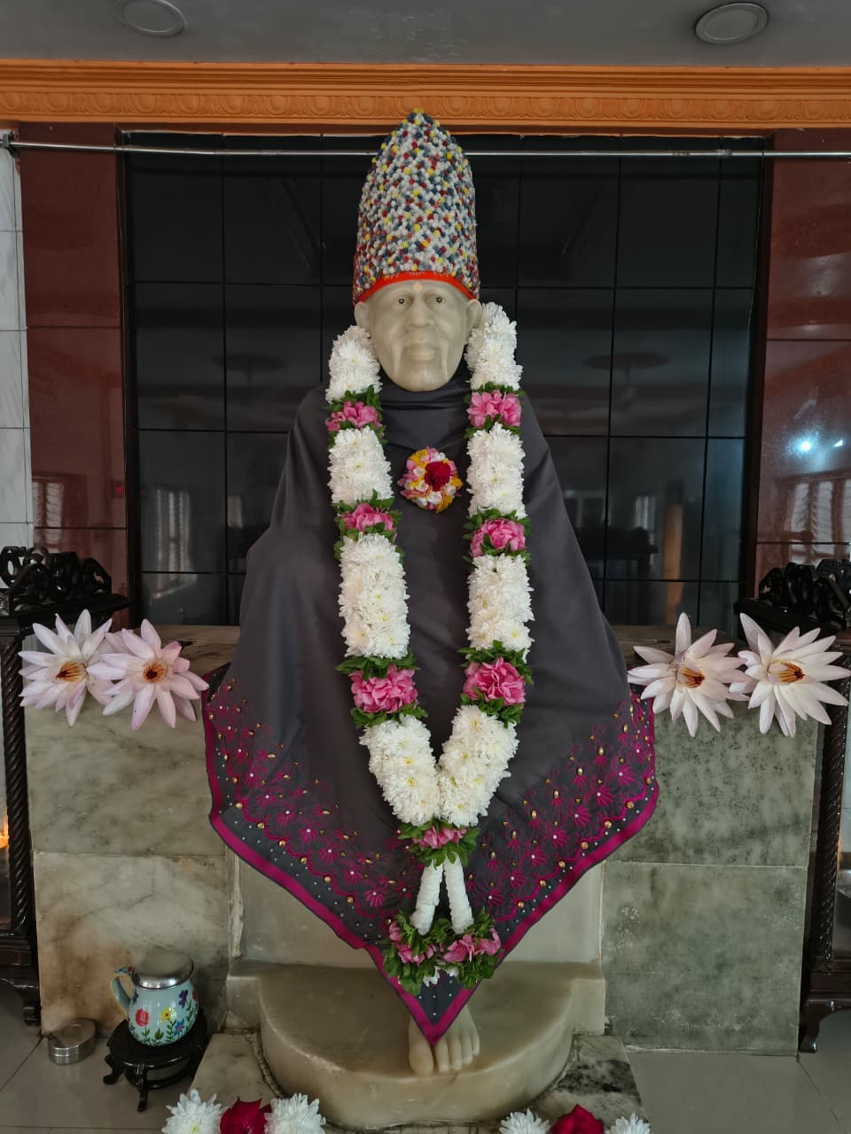 Murti in a grey shawl with a multicolor confetti-pattern crown and a white-and-pink floral garland