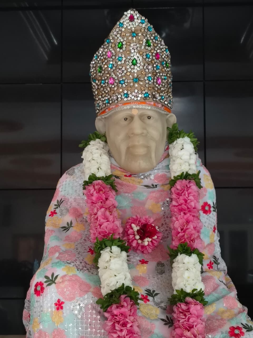 Murti in a pastel floral-print robe with a jeweled silver crown and a pink-and-white garland