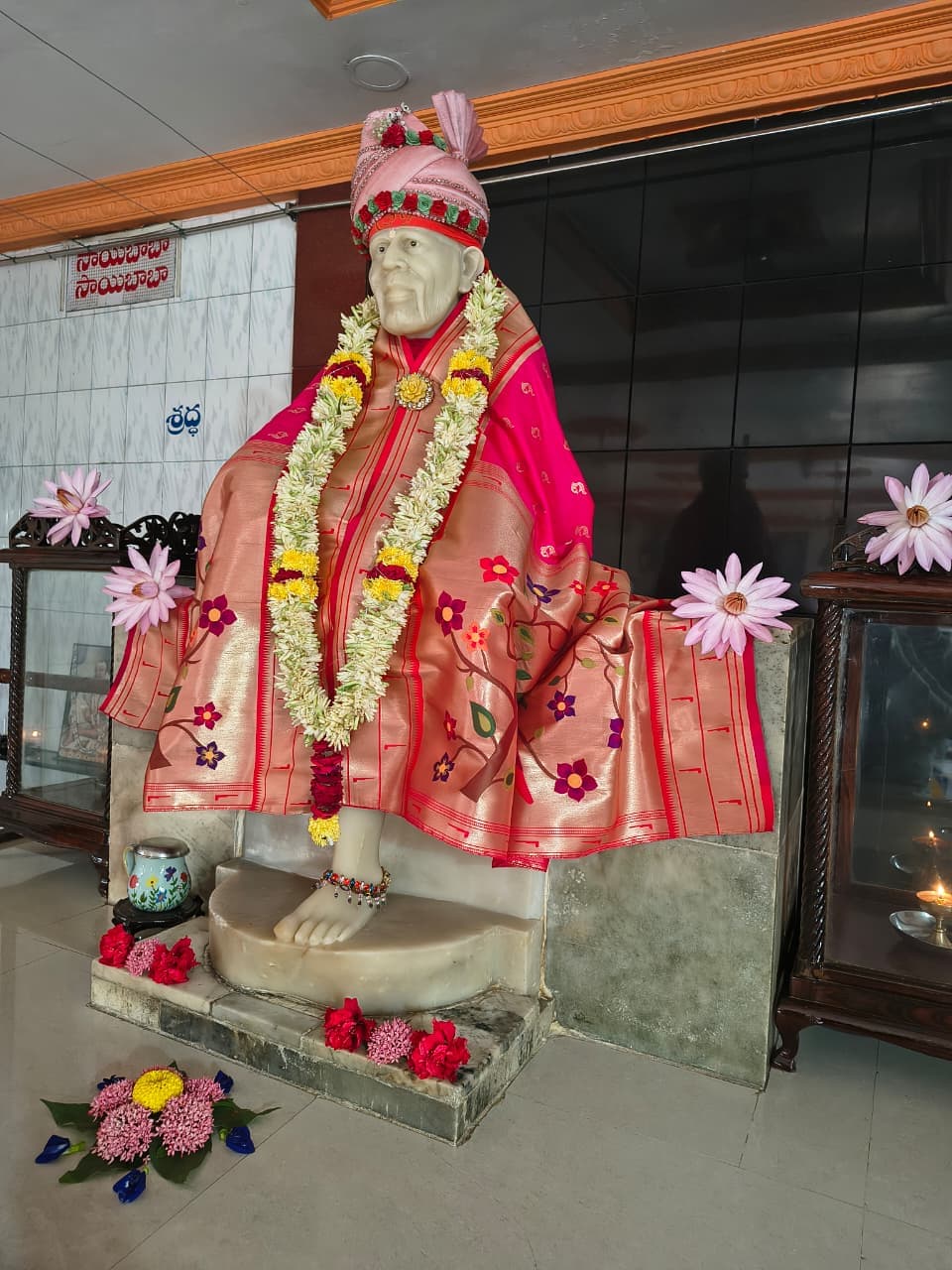 Murti in a coral-and-gold brocade robe with a pink jeweled turban, photographed at an angle