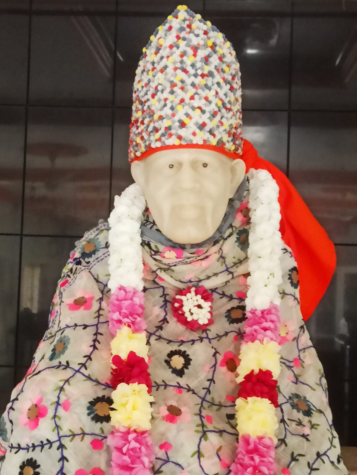 Murti in a cream floral-embroidered shawl with a red cape and a multicolor confetti crown