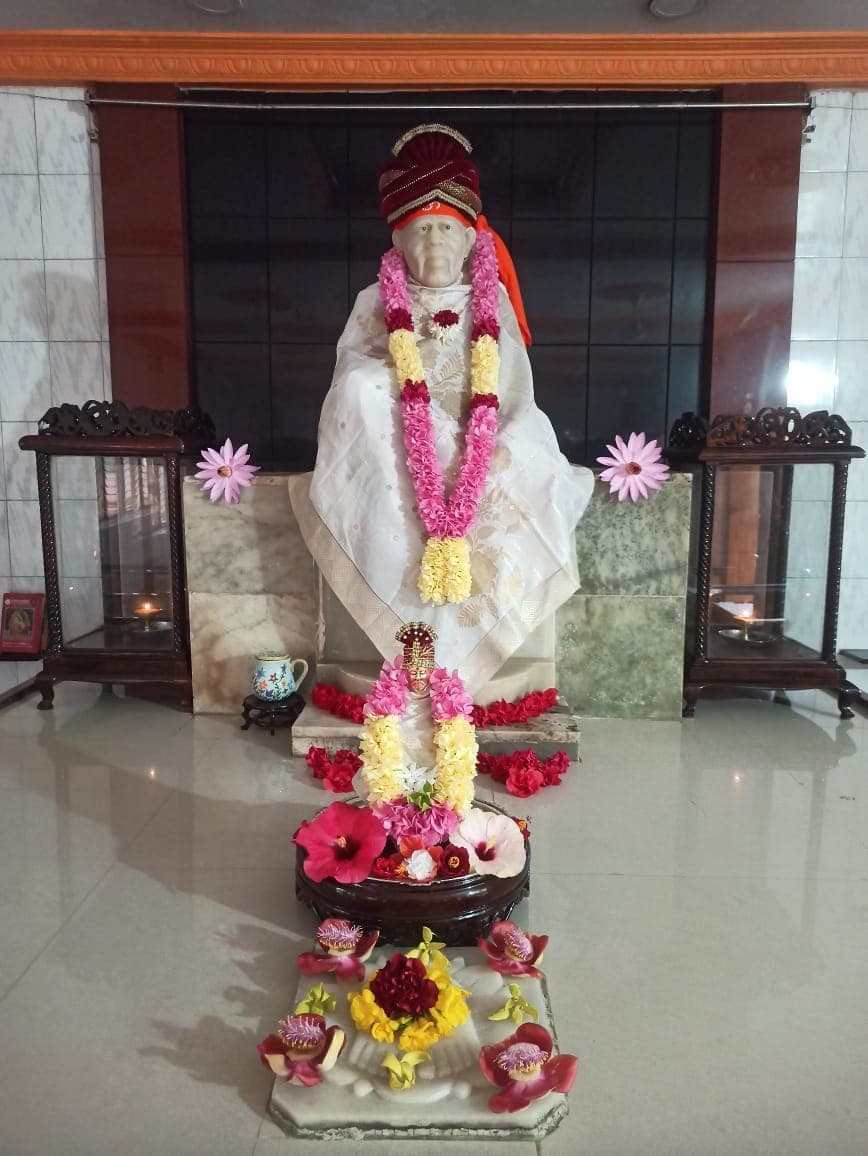 Murti in a white-and-cream floral shawl with a maroon turban, a small companion murti with hibiscus flowers in front