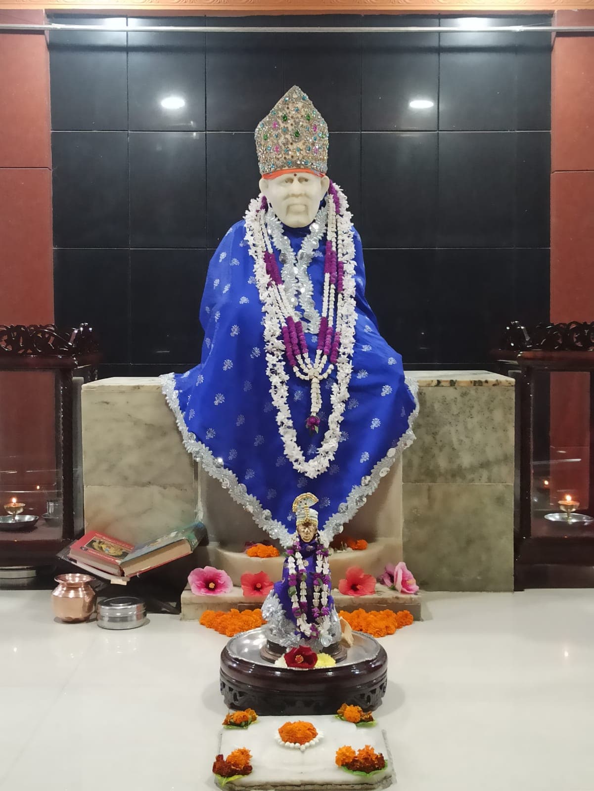 Murti in a royal blue robe with a silver floral pattern, a jeweled crown, and a small companion murti in front