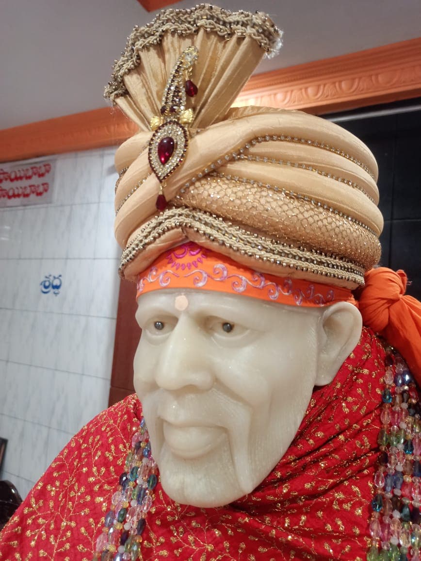 Murti in a red robe with multicolor beaded strands, photographed close-up in profile with a gold jeweled turban