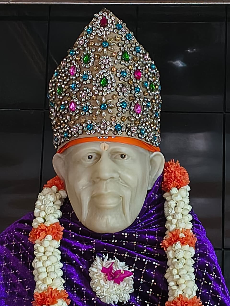Murti in a deep purple velvet robe with a jeweled multicolor crown and a white-and-orange marigold garland