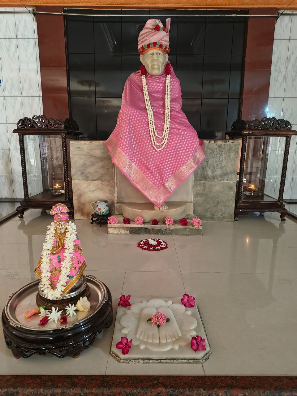 Murti in a pink diamond-pattern silk robe with a beaded floral crown and a white pearl-strand garland