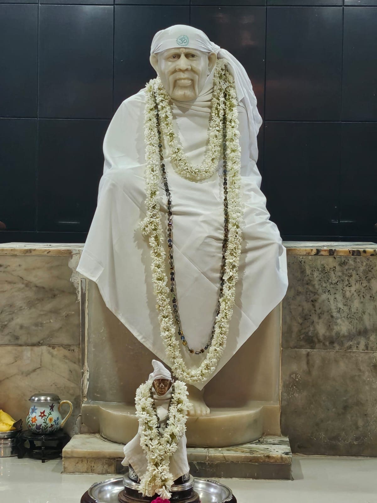 The white marble Sai Baba murti, draped in white cloth and garlanded, with a smaller matching murti at its feet