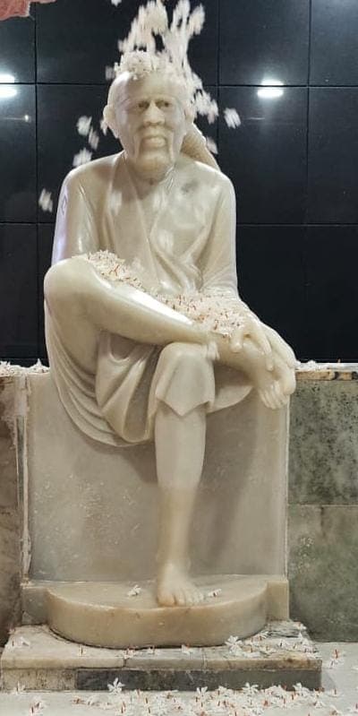 The unconsecrated white marble Sai Baba murti, seated, being showered with flower petals