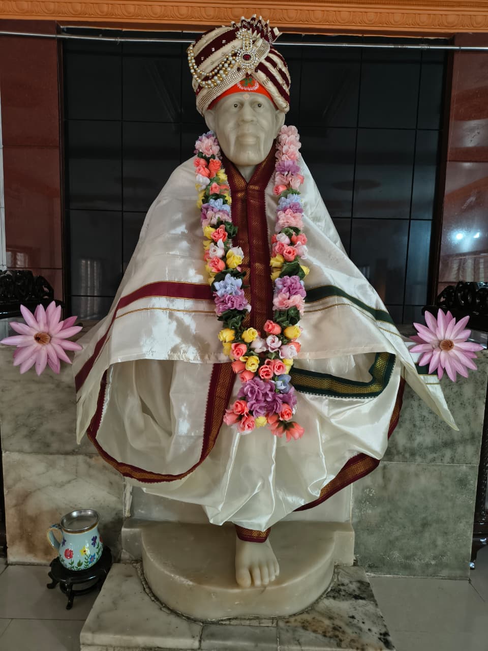 The murti in a white shawl and pearled crown, garlanded with colorful flowers